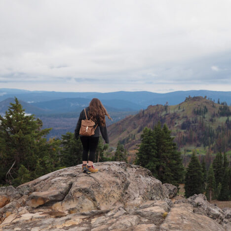 girl on a rock with views of mountains and trees in the background