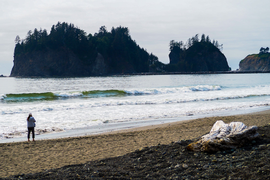 a woman walking along the beach with james island and waves behind her