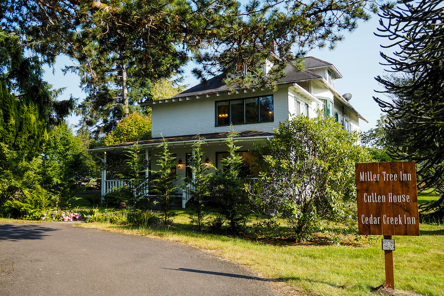 a two-story house with a wrap-around porch with a sign in front that says "Miller Tree Inn / Cullen House / Cedar Creek Inn"