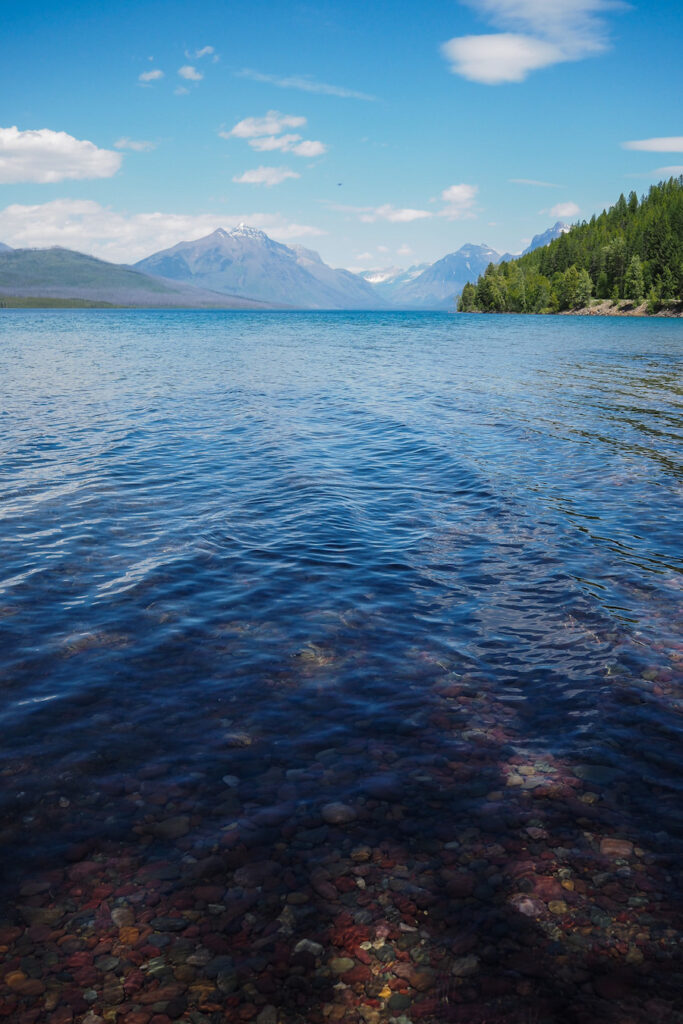 a lake with clear enough water to see colorful pebbles on the bottom in Glacier National Park