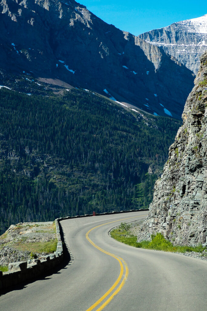 a curvy road with a view of mountains in Glacier National Park