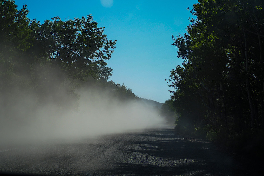 a car leaving a trail of dust while driving on the dirt road in Glacier National Park