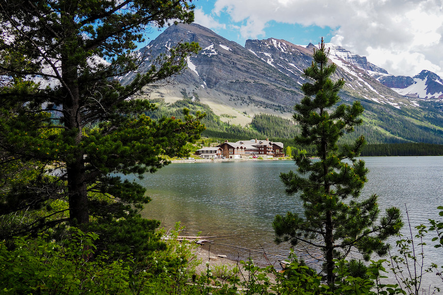 view of pine trees and the Many Glacier Hotel in the background, across from a lake
