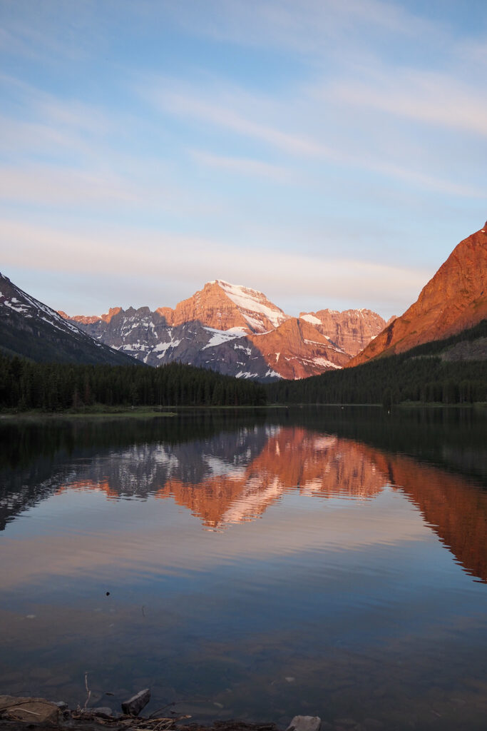 a sunrise making mountains colorful with a reflection on the lake in Glacier National Park