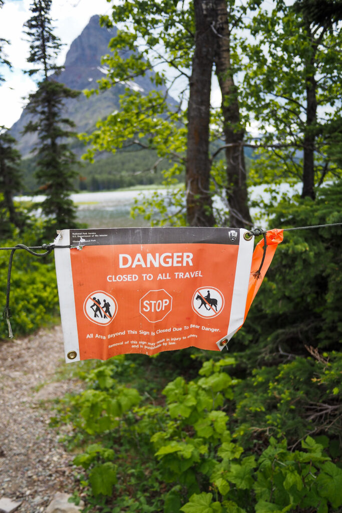 a sign that says "Danger Closed to All Travel: Stop: All Areas Beyond This Sign Closed to Bear Danger" hanging in front of a trail