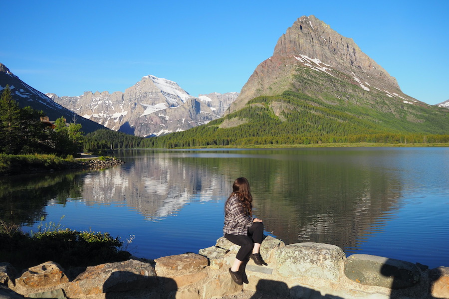 a woman sitting on a wall looking behind her to the lake in Glacier National Park