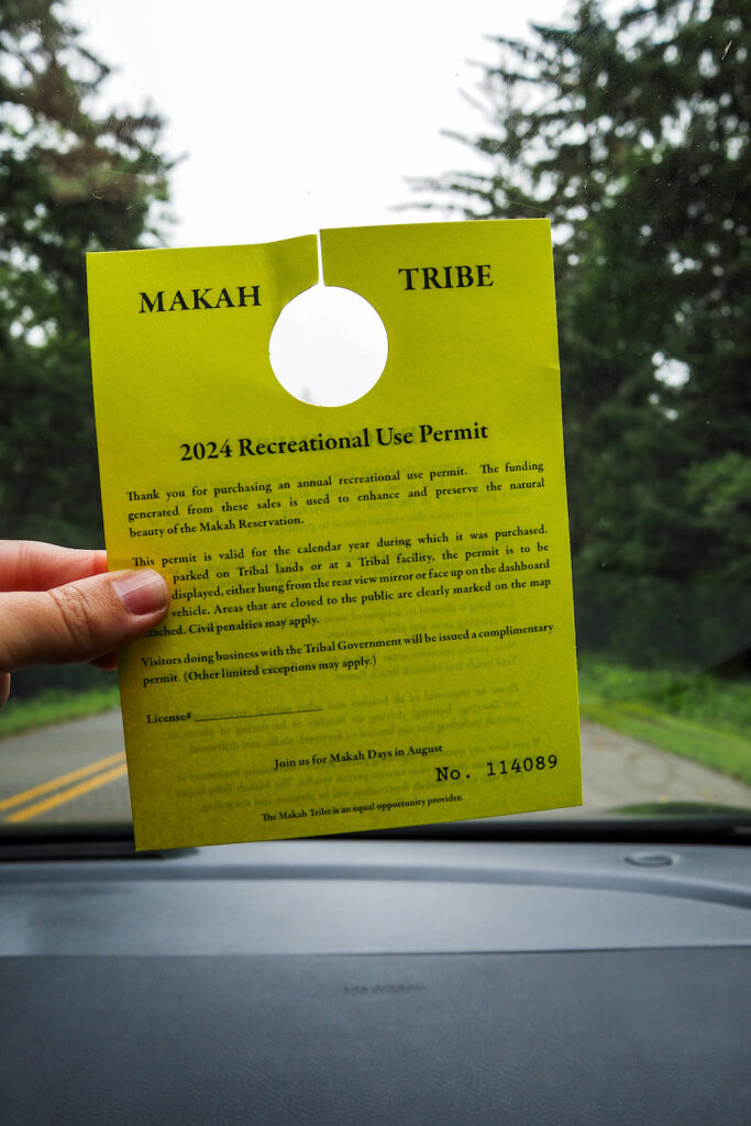 a hand holding up a yellow paper with a hole at the top to hang in a car rear-view mirror. The paper says "2024 Recreational Use Permit" at the top
