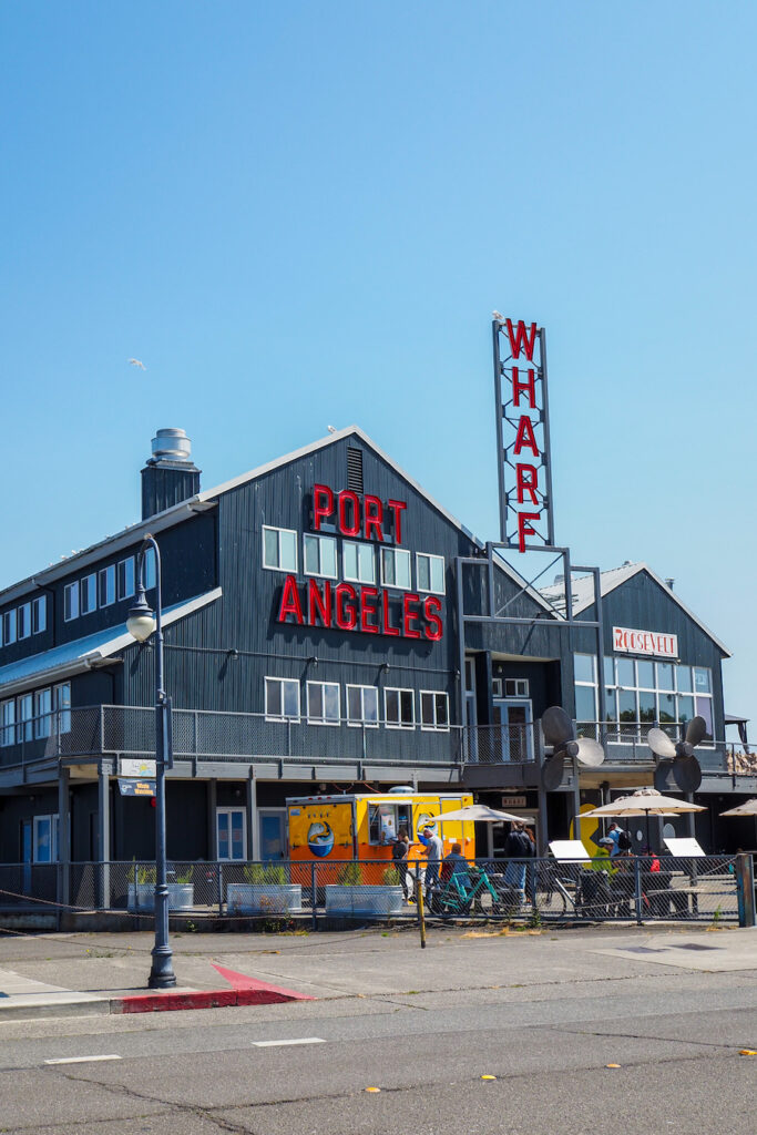 a wooden building with red letters on it that say PORT ANGELES WHARF