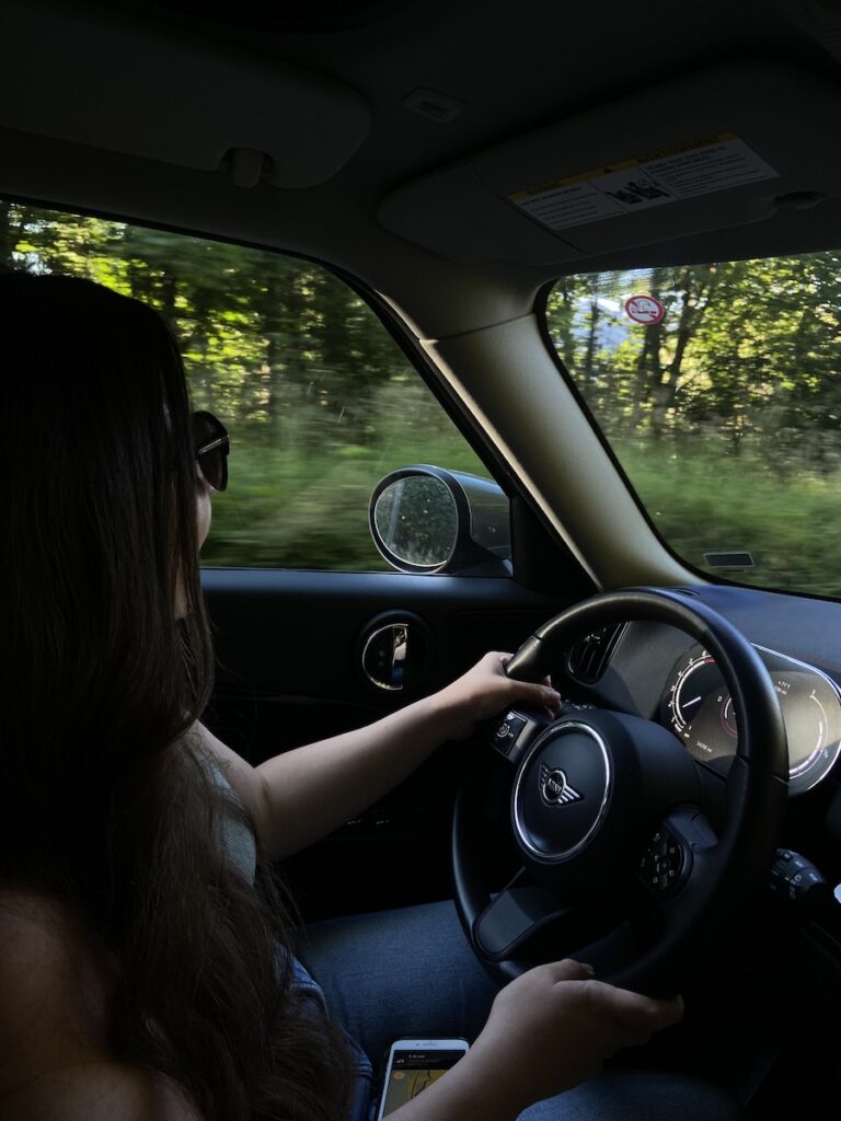 girl driving a on a street with lots of trees blurred out the window