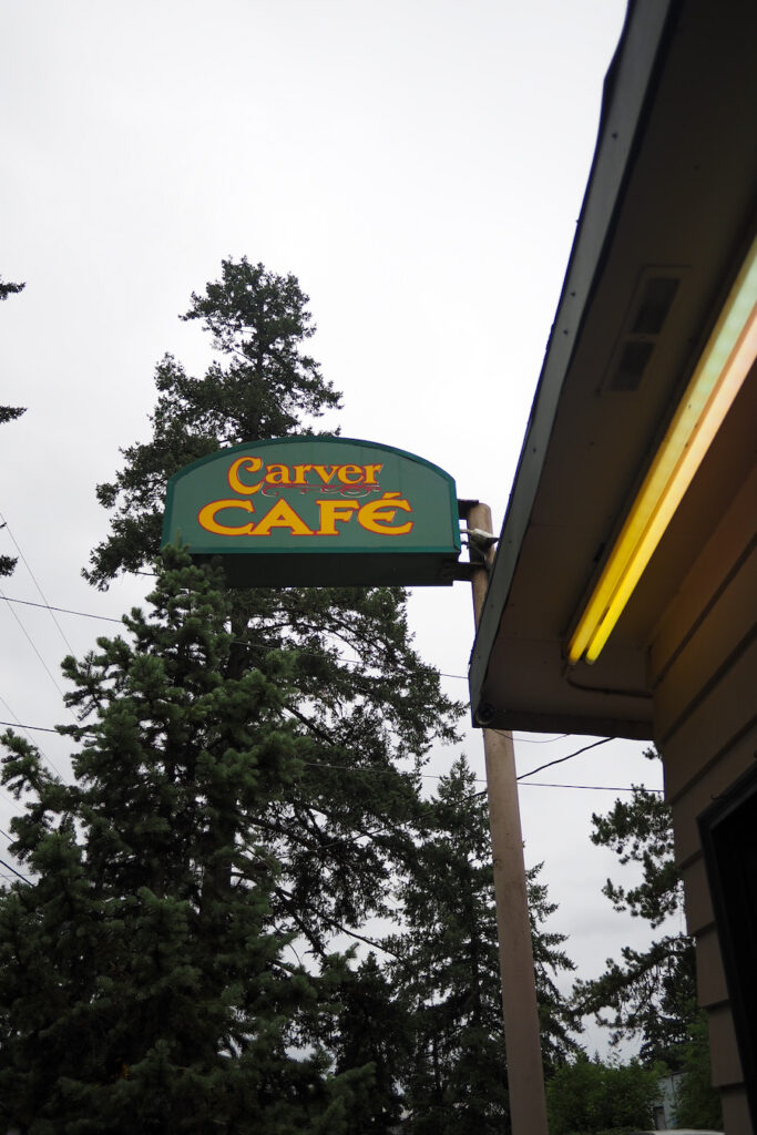 sign that says "Carver Cafe" outside on the storefront with pine trees behind it
