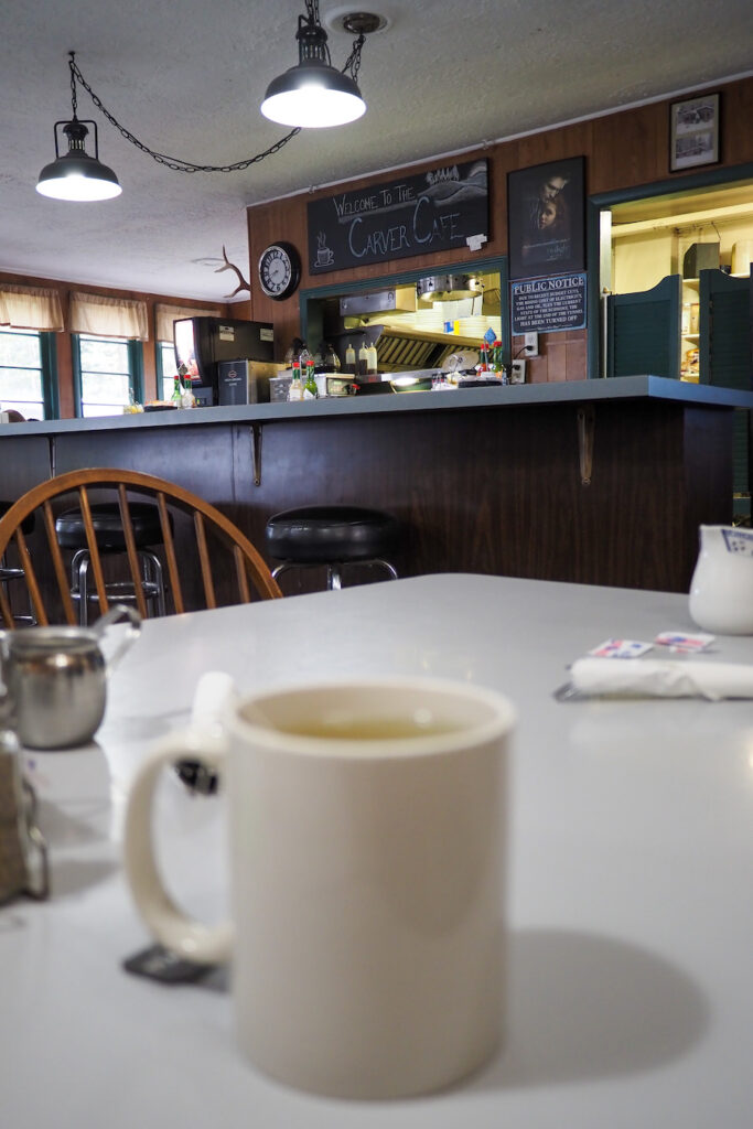 a white mug on a table in a diner with a sign in the background that says "Carver Cafe"