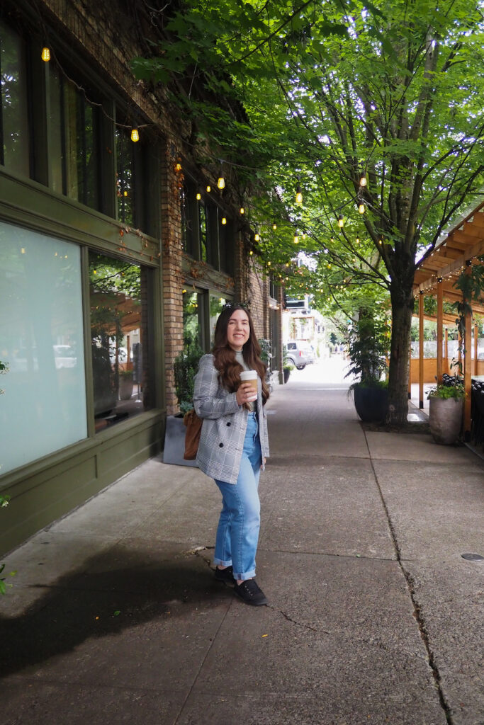 girl standing on a sidewalk in the Northwest District in Portland holding a warm beverage