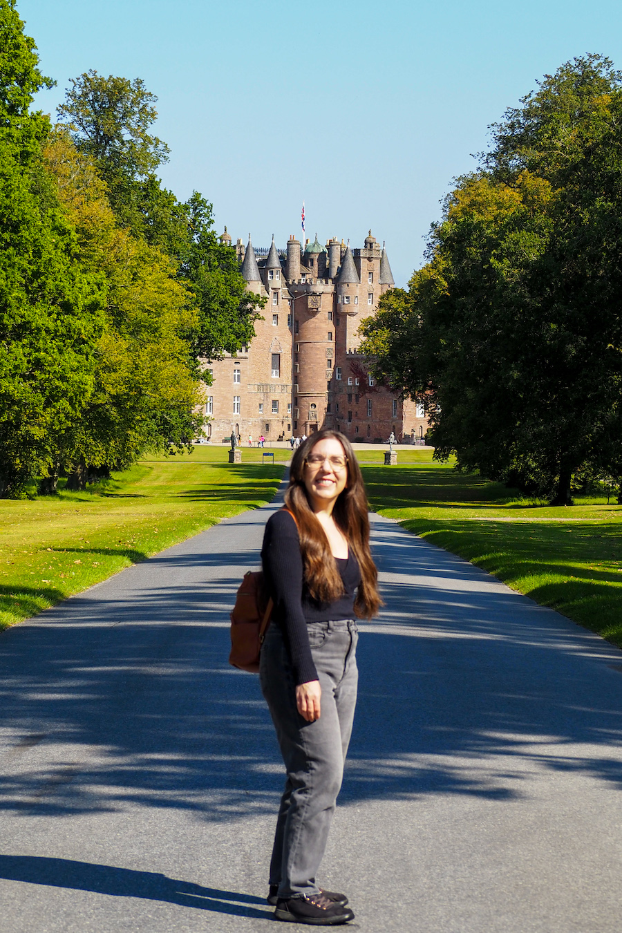 a young woman standing in the middle of the road with Glamis Castle in the back