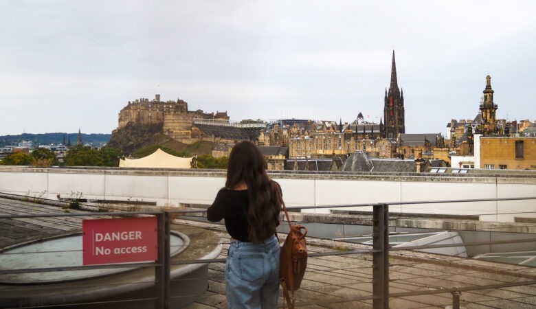 A person stands on a rooftop overlooking Edinburgh Castle and the city skyline, with a DANGER No access sign in the foreground.